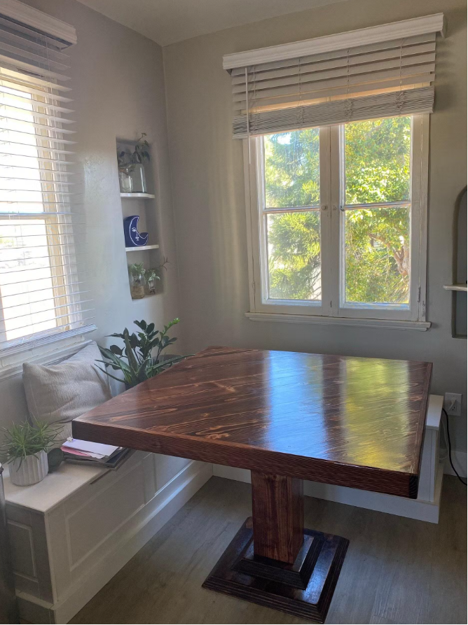 Wooden dining table in a room with a window and shelves.