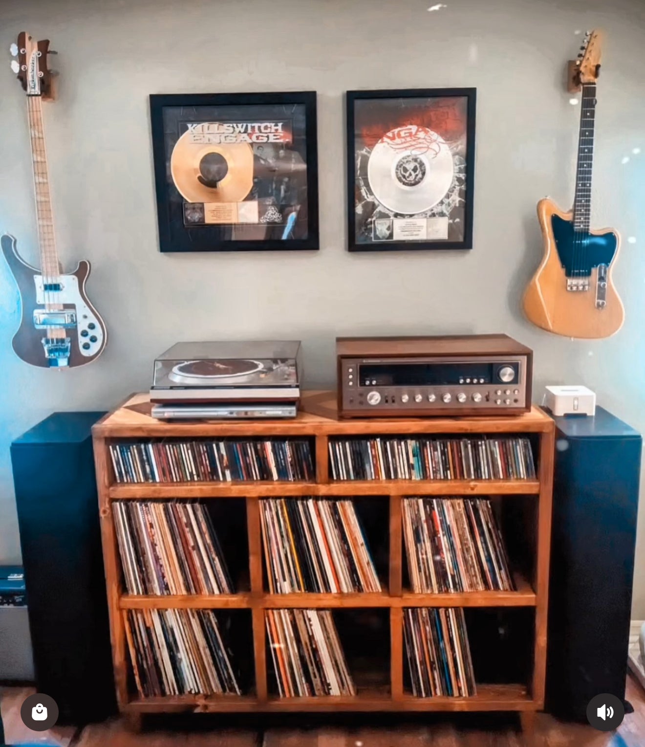 Wooden record player console with vinyl records, framed records on the wall, and guitars.